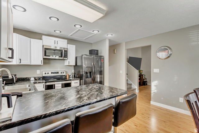 933 South Freedom Boulevard, Unit 7 Provo, UT 84601 - Photo 7 of 23 Kitchen with stainless steel appliances, a kitchen bar, white cabinets, and light wood finished floors