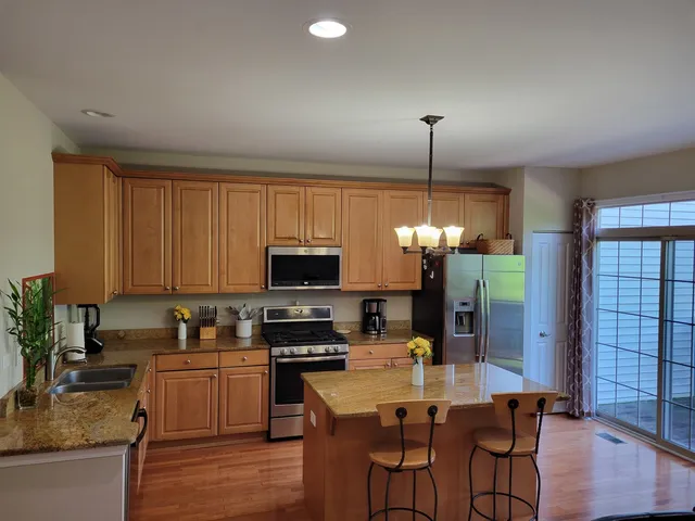 a kitchen with stainless steel appliances granite countertop a stove top oven a sink dishwasher a dining table and chairs with wooden floor