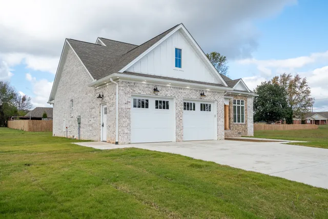 a view of a white house next to a yard with big trees