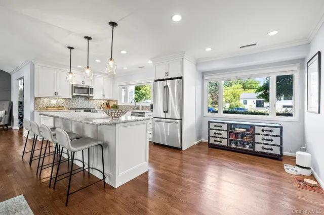 a kitchen with stainless steel appliances kitchen island granite countertop a stove a refrigerator a sink a dining table and chairs with wooden floor