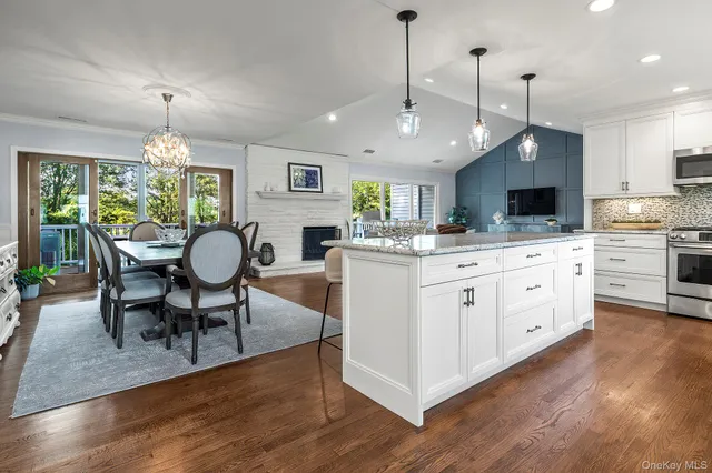 a large white kitchen with granite countertop a stove a sink a dining table and chairs with wooden floor