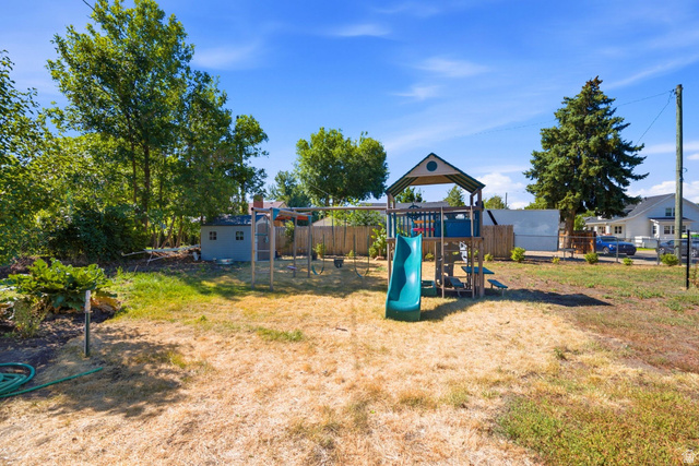 310 East 600 South Centerville, UT 84014 - Photo 27 of 41 Spacious backyard featuring a wooden play structure with a slide, a swing set, mature trees, and a storage shed