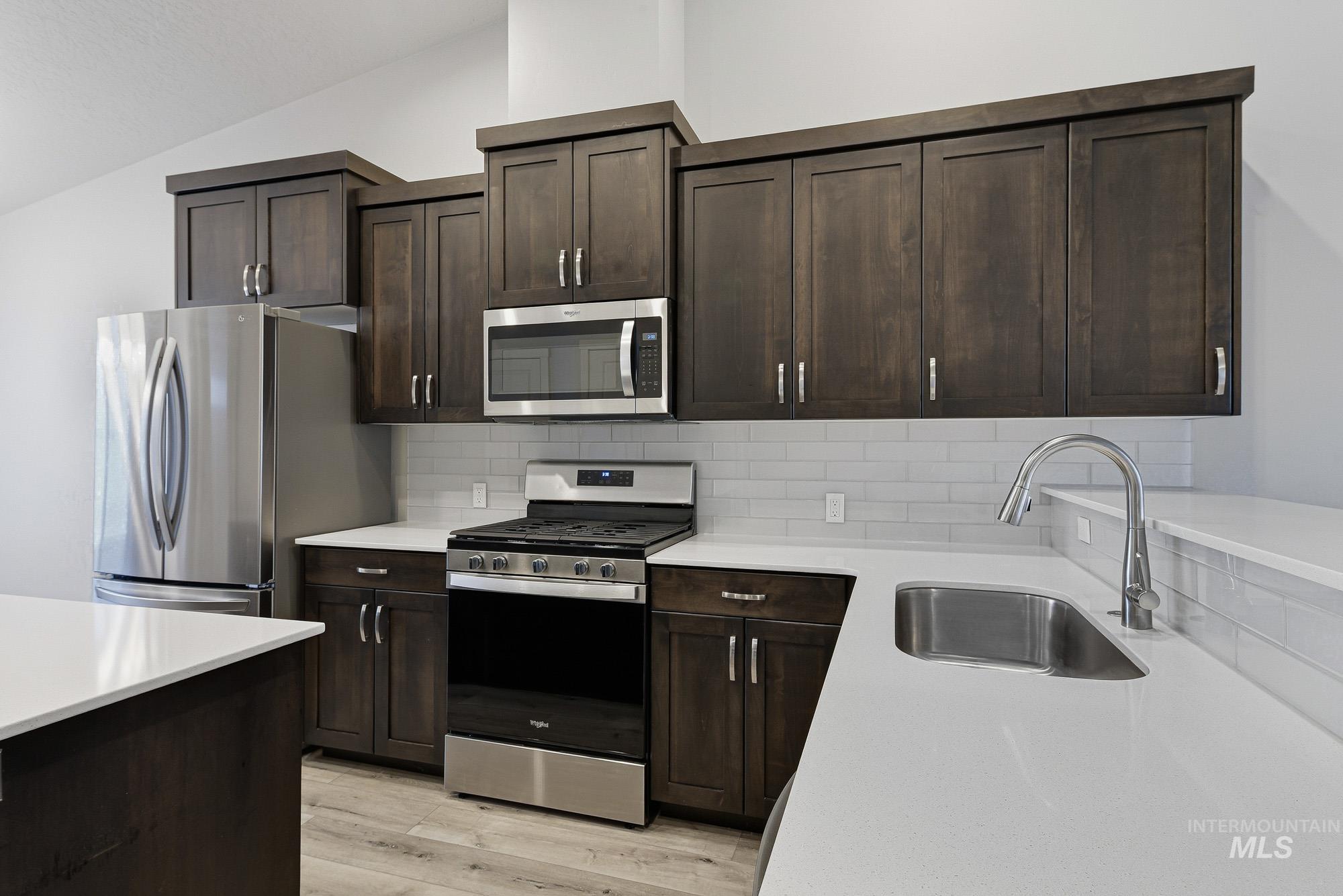 3065 North Summerbrook Avenue Meridian, ID 83646 - Photo 11 of 33 Kitchen featuring stainless steel appliances, dark wood finish cabinets, backsplash, light wood-type flooring, and light stone counters