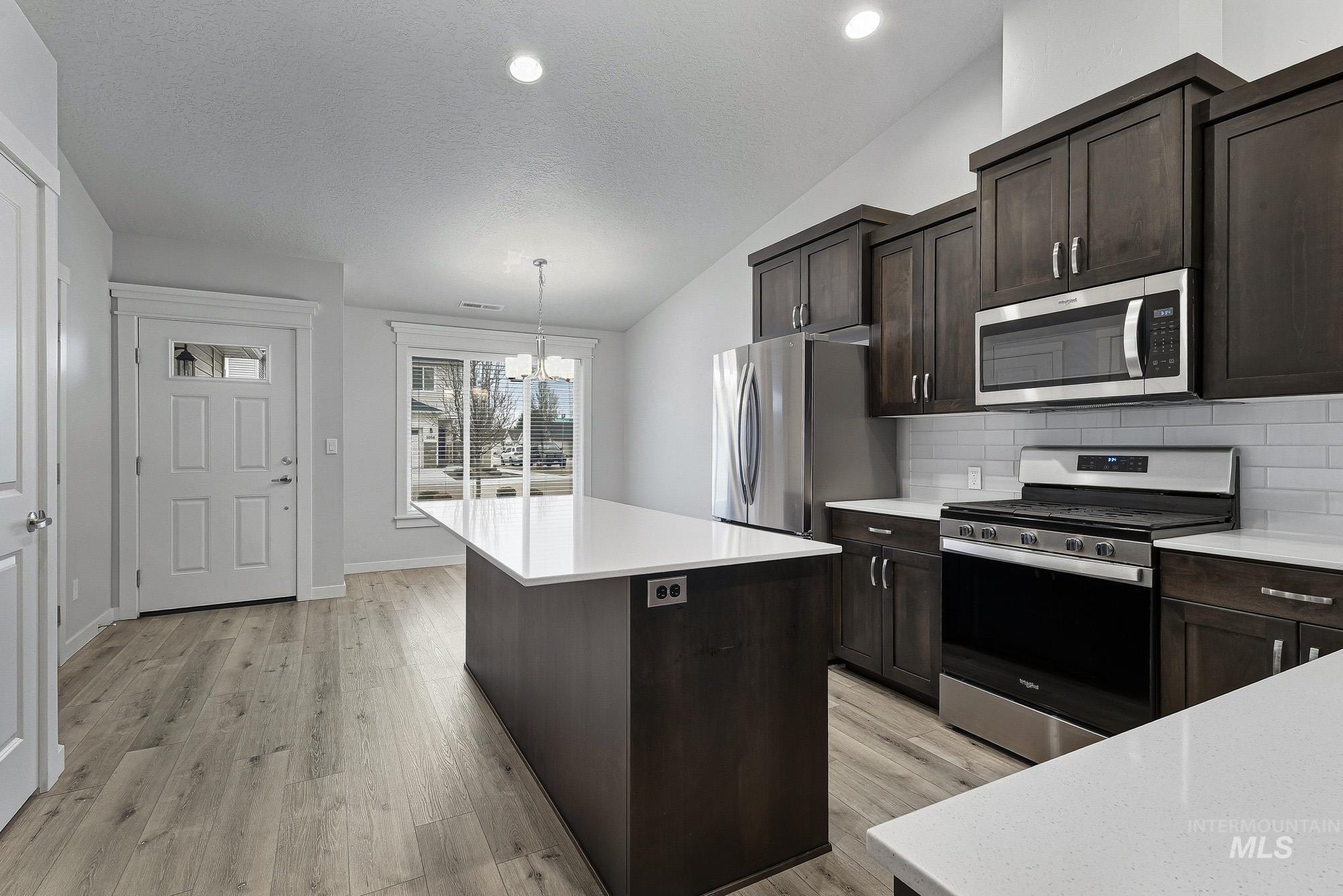3065 North Summerbrook Avenue Meridian, ID 83646 - Photo 12 of 33 Kitchen featuring dark wood finish cabinets, stainless steel appliances, light wood-style floors, a kitchen island, and backsplash
