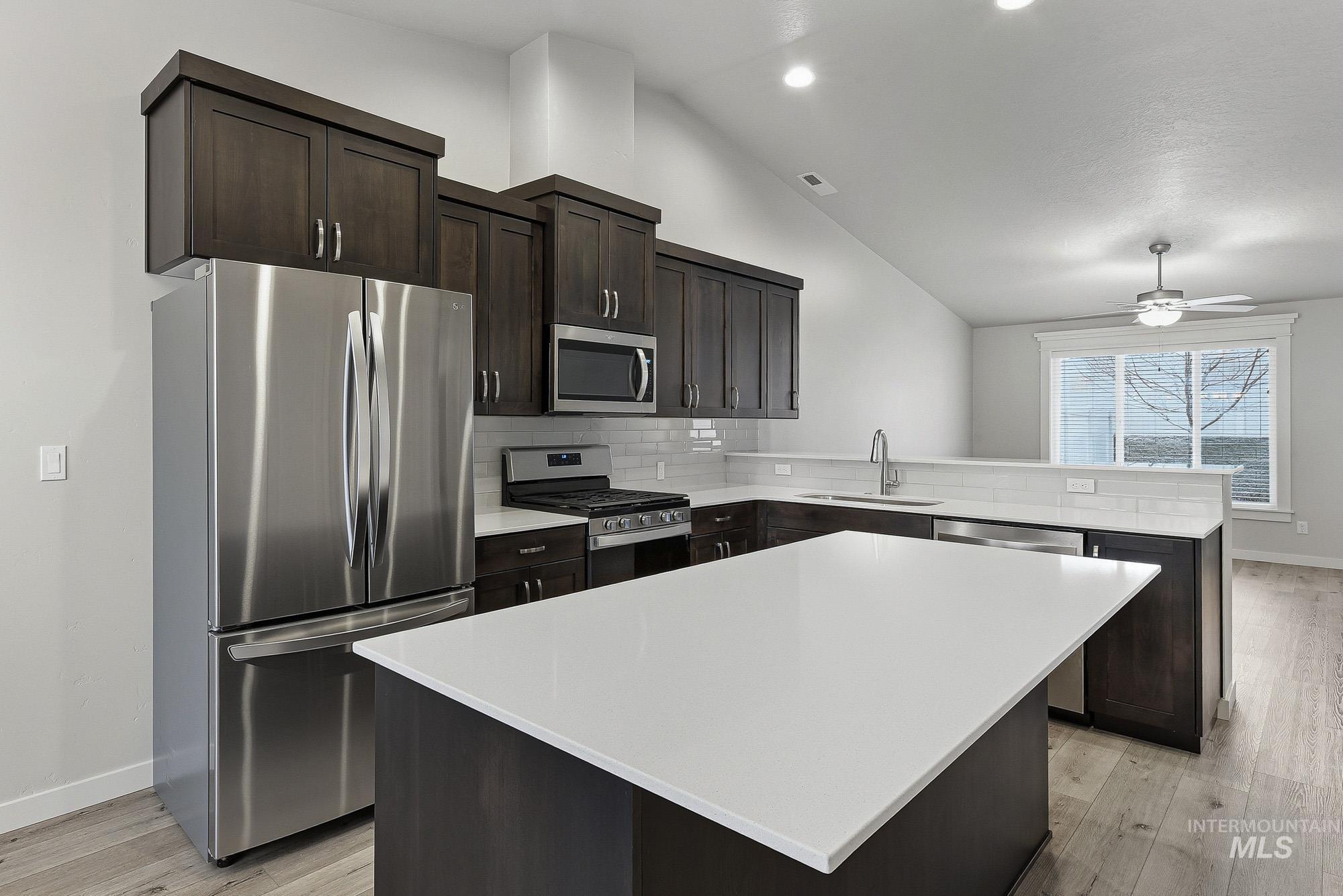 3065 North Summerbrook Avenue Meridian, ID 83646 - Photo 6 of 33 Kitchen featuring stainless steel appliances, dark wood finish cabinets, lofted ceiling, tasteful backsplash, and light wood-style flooring