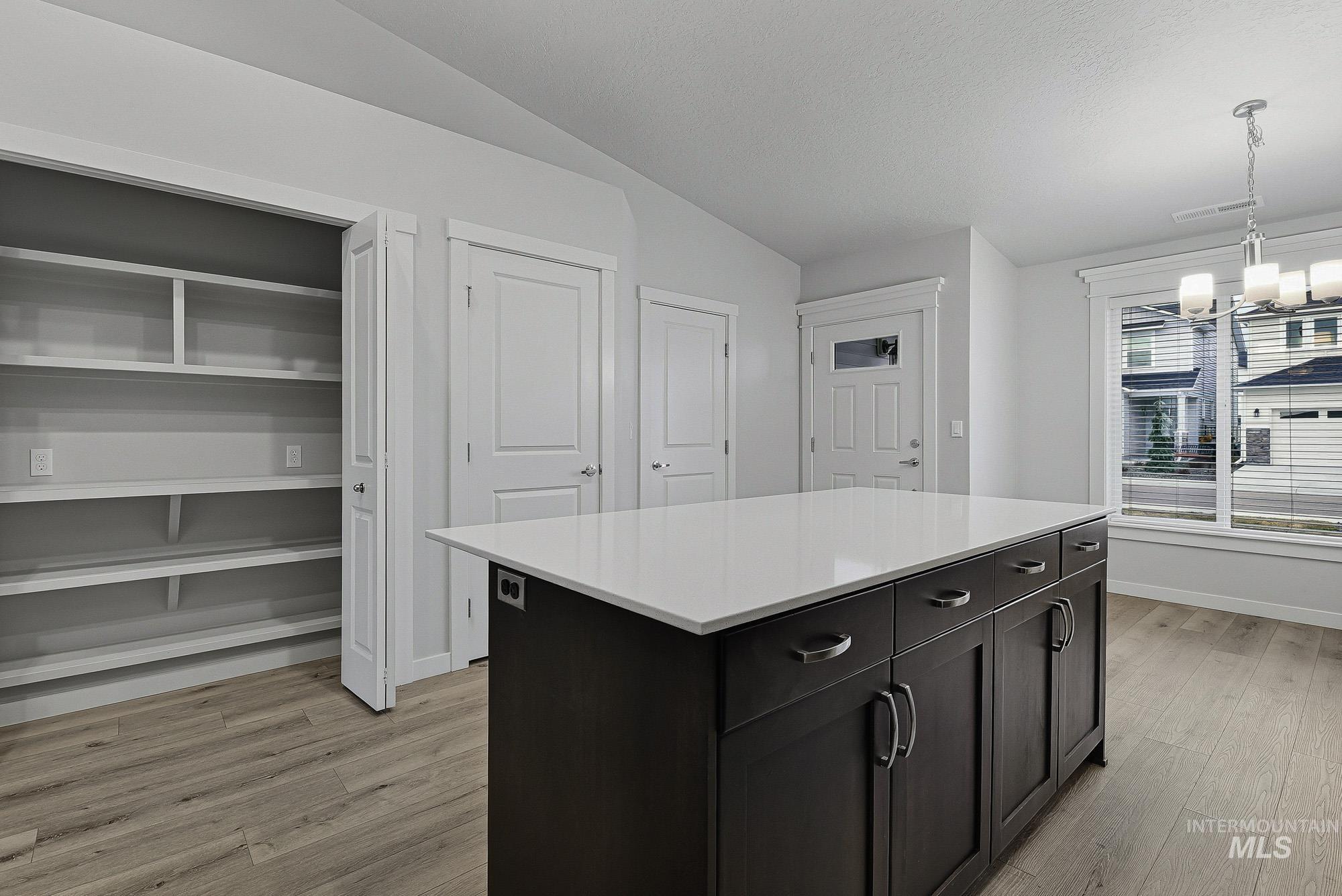3065 North Summerbrook Avenue Meridian, ID 83646 - Photo 8 of 33 Kitchen with a kitchen island, lofted ceiling, light wood finished floors, suspended lighting, and dark cabinetry
