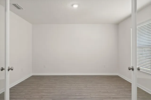 a view of an empty room with wooden floor and a window