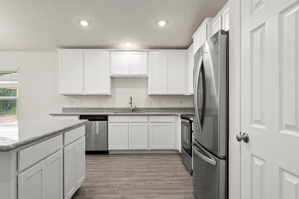 a kitchen with stainless steel appliances granite countertop a refrigerator a sink and white cabinets
