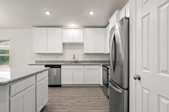 a kitchen with stainless steel appliances granite countertop a refrigerator a sink and white cabinets