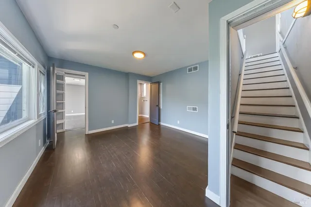 a view of an empty room with wooden floor and stairs