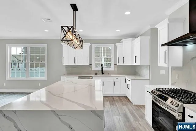 a kitchen with granite countertop a stove a sink dishwasher a refrigerator and white cabinets with wooden floor