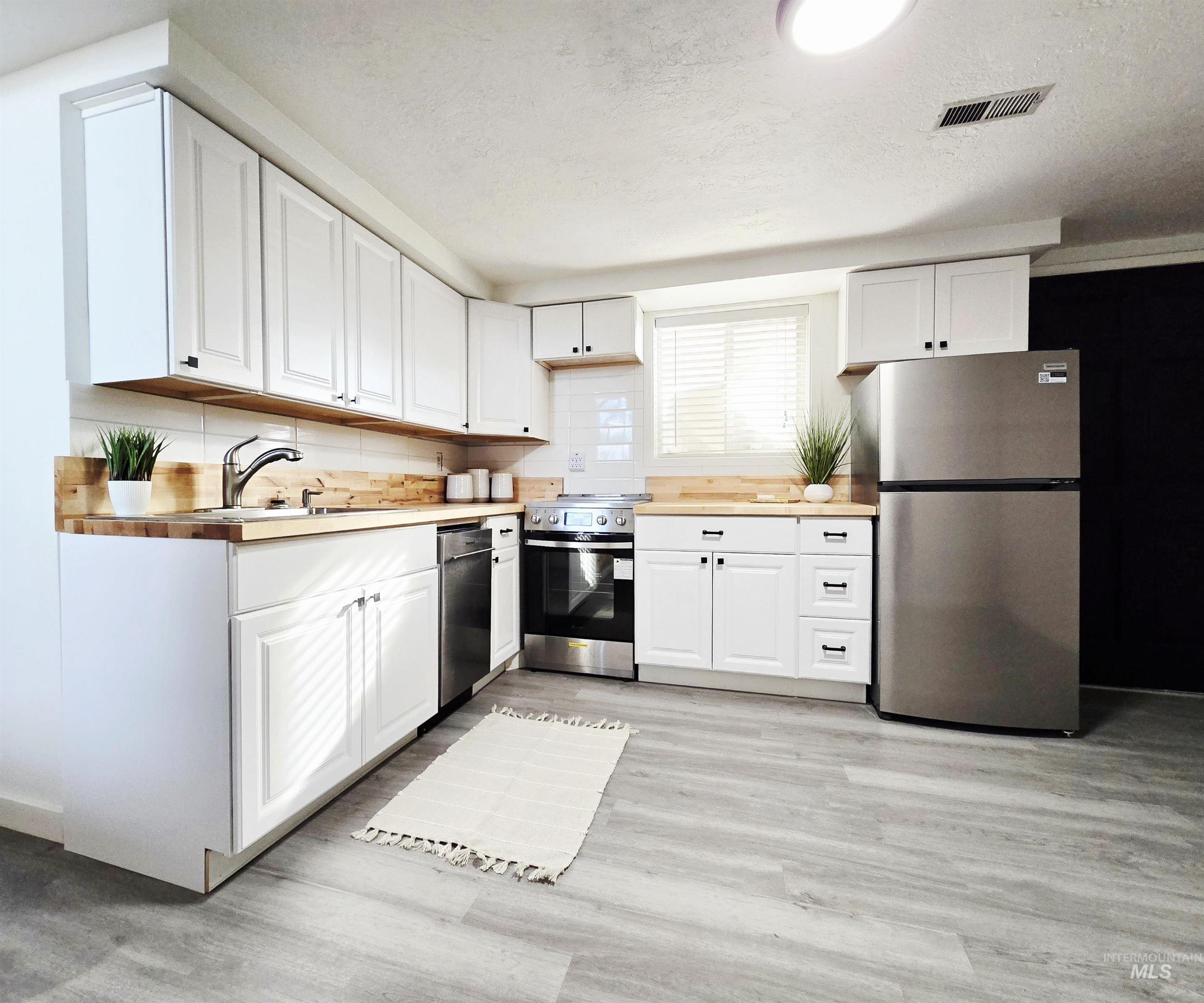 728 Northwest 8th Street Meridian, ID 83642 - Photo 5 of 18 Kitchen with stainless steel appliances, white cabinets, light wood-type flooring, and a textured ceiling