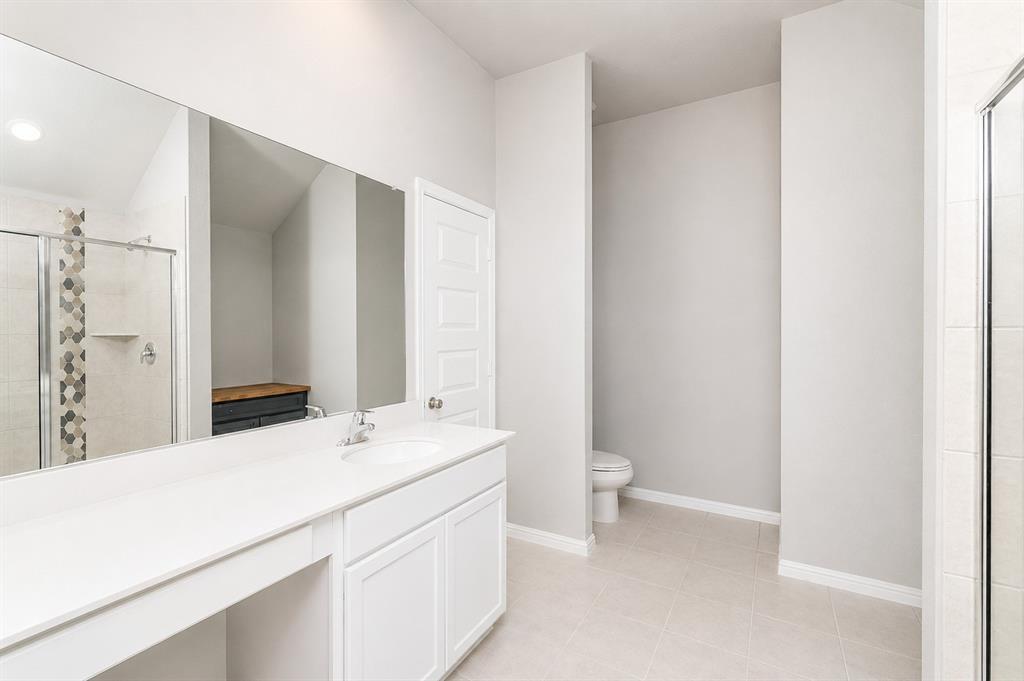 3344 Duncan Way Corinth, TX 76210 - Photo 17 of 38 Contemporary bathroom featuring a spacious vanity with integrated sink, a large wall-mounted mirror, and a glass-enclosed shower with decorative hexagonal tile accents
