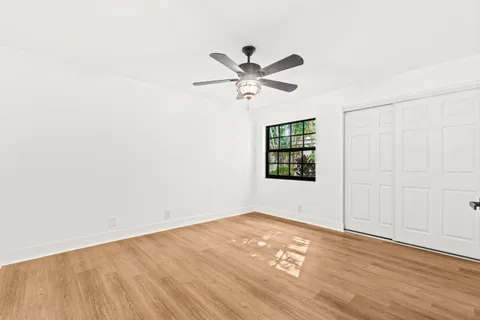 an empty room with wooden floor ceiling fan and window