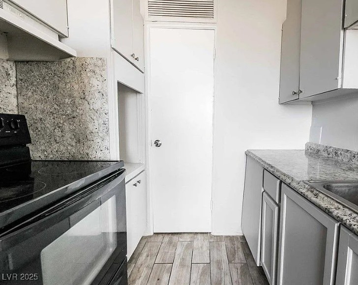 239 West Cleveland Avenue, Unit 1 Las Vegas, NV 89102 - Photo 5 of 12 Kitchen with black range with electric cooktop, under cabinet range hood, gray cabinets, wood tiled floors, and tasteful backsplash