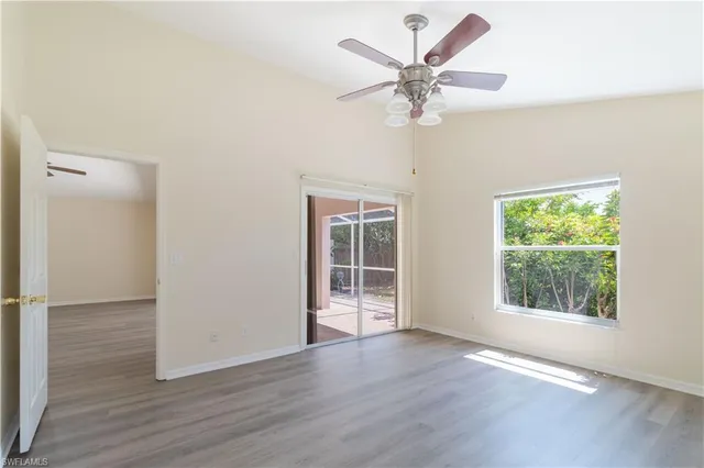 an empty room with wooden floor chandelier fan and windows