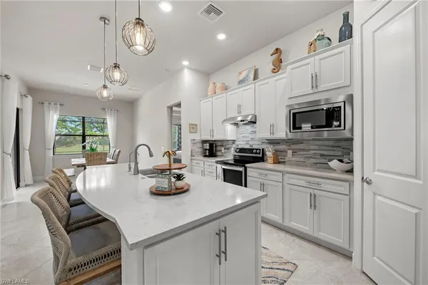 a kitchen with stainless steel appliances kitchen island granite countertop a sink dishwasher a stove a refrigerator a microwave oven with white cabinets and wooden floor