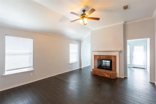 an empty room with wooden floor a fireplace a ceiling fan and windows