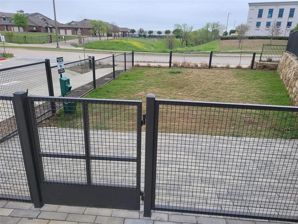 2700 Old Denton Road, Unit 2238 Carrollton, TX 75007 - Photo 21 of 21 Fenced outdoor area featuring a mesh gate, paver stone walkway, and a landscaped grassy section