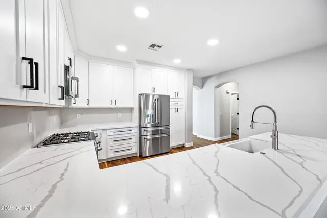 a kitchen with stainless steel appliances kitchen island granite countertop a stove a sink and a refrigerator with white cabinets