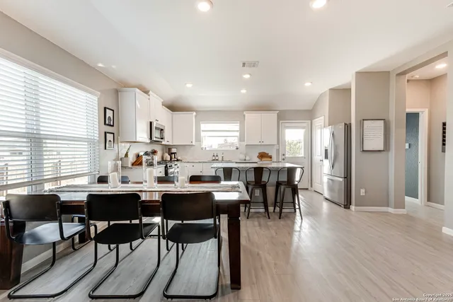 a room with stainless steel appliances kitchen island granite countertop a dining table chairs and wooden floor