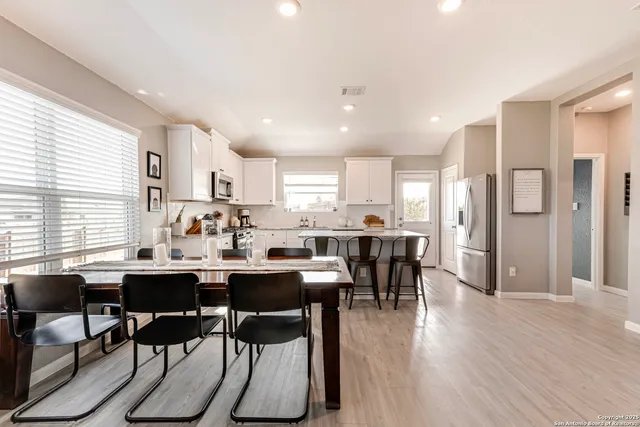 a room with stainless steel appliances kitchen island granite countertop a dining table chairs and wooden floor