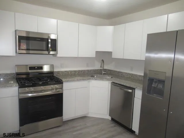 a kitchen with granite countertop white cabinets stainless steel appliances and a sink
