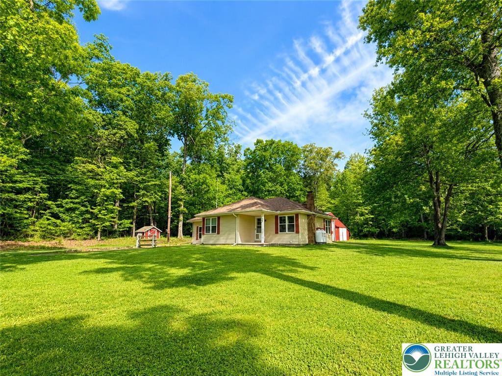 4995 Mountain Road Slatington, PA 18080 - Photo 4 of 30 A cream-colored home with red shutters is nestled amongst verdant trees on a spacious lawn.
