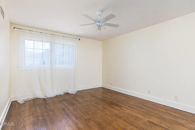 an empty room with wooden floor fan and windows