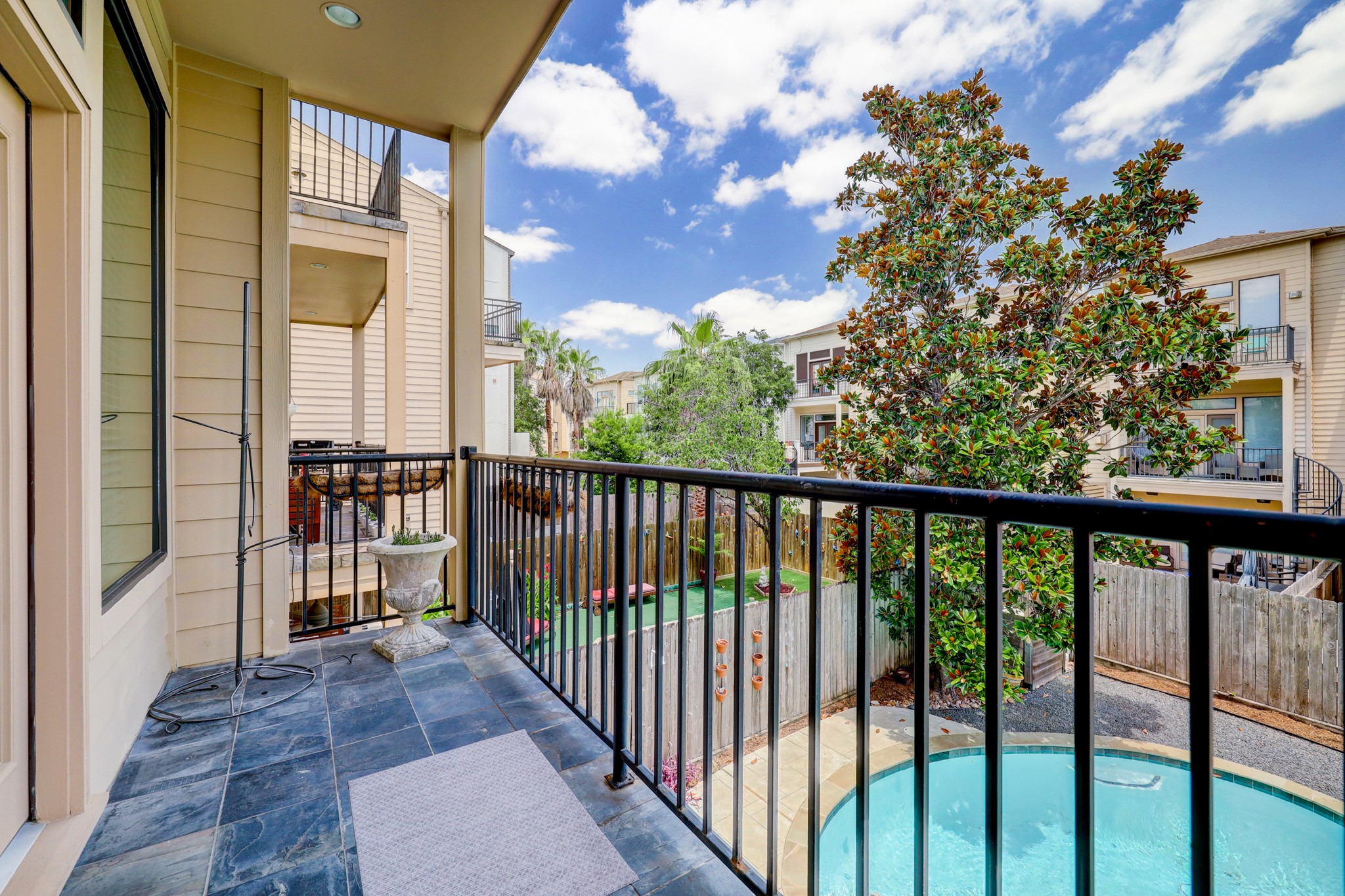 5202 Rose Street, Unit B Houston, TX 77007 - Photo 12 of 40 A cozy balcony with slate flooring overlooks a backyard featuring a round pool and lush greenery. Ideal for relaxing or entertaining, it offers a peaceful view of neighboring townhouses and trees under a bright, blue sky.