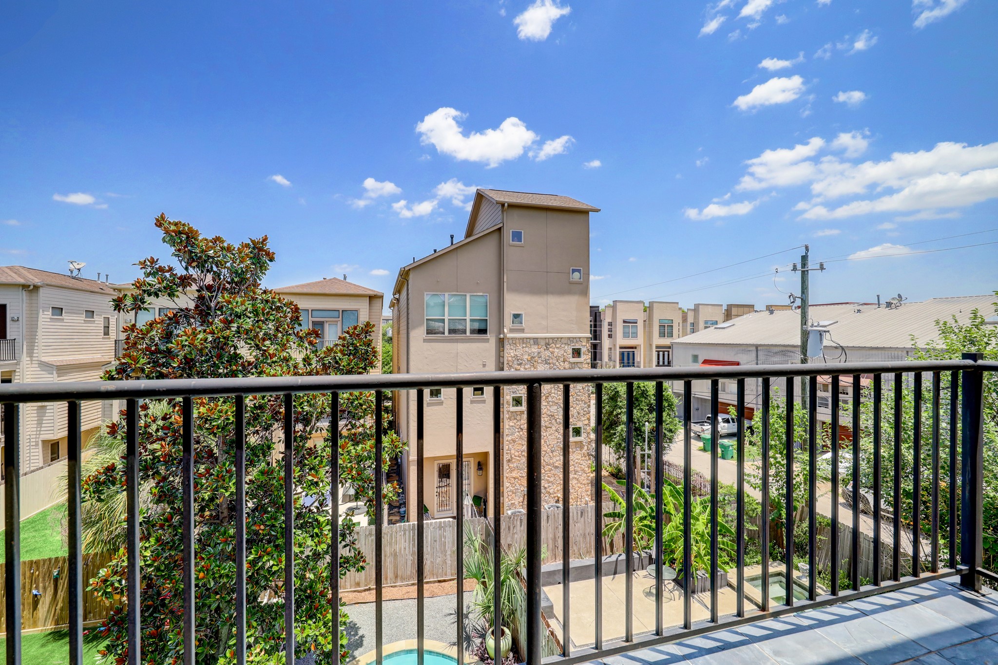 5202 Rose Street, Unit B Houston, TX 77007 - Photo 13 of 40 This photo showcases a modern balcony view featuring nearby houses. The area includes a mix of greenery and urban elements, with a visible pool and clear blue skies, providing a pleasant and inviting atmosphere.