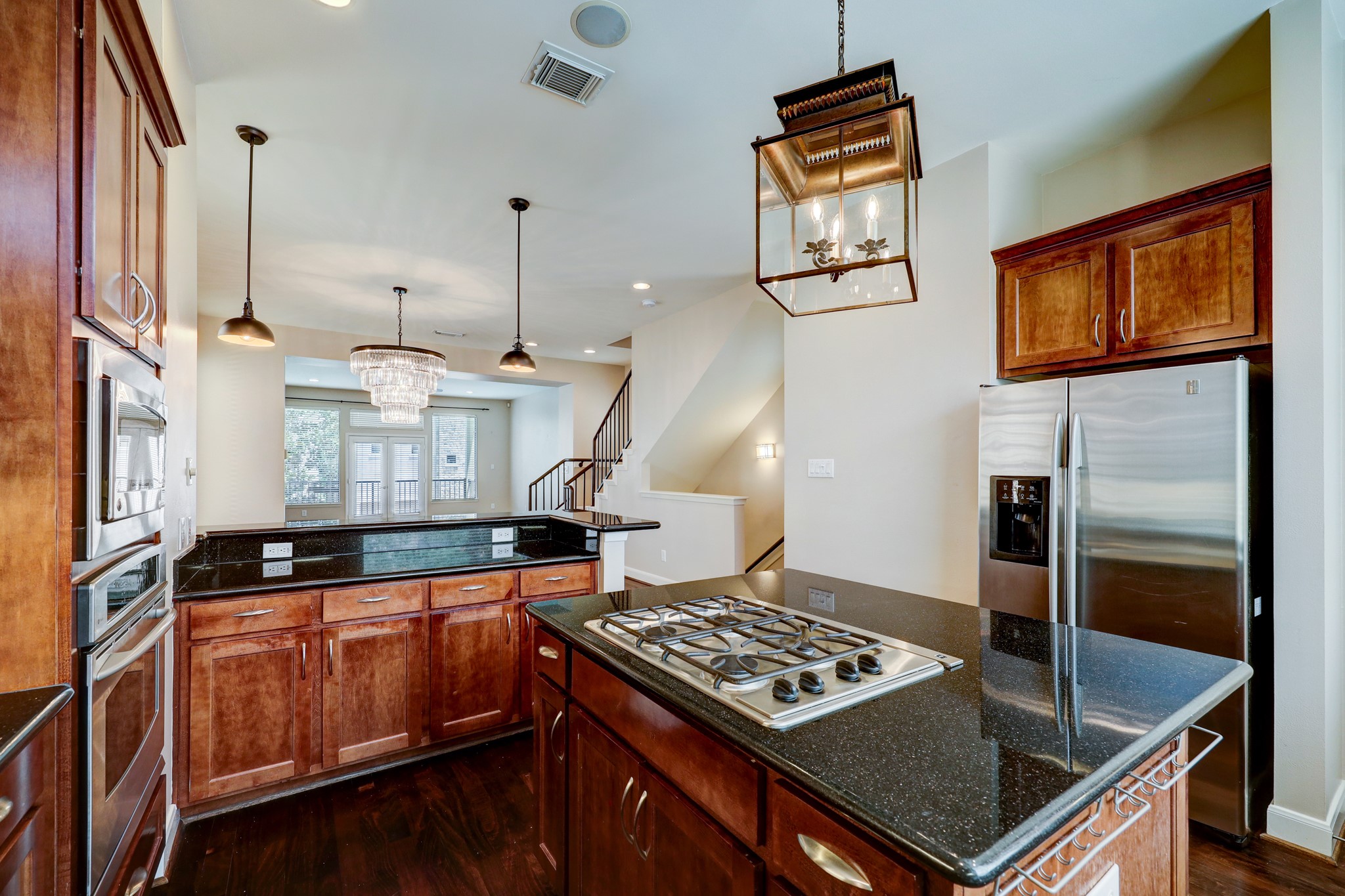5202 Rose Street, Unit B Houston, TX 77007 - Photo 2 of 40 This kitchen features elegant dark wood cabinetry, granite countertops, a central island with a gas cooktop, stainless steel appliances, and stylish pendant lighting. The open layout flows into a bright living area with large windows and a staircase.