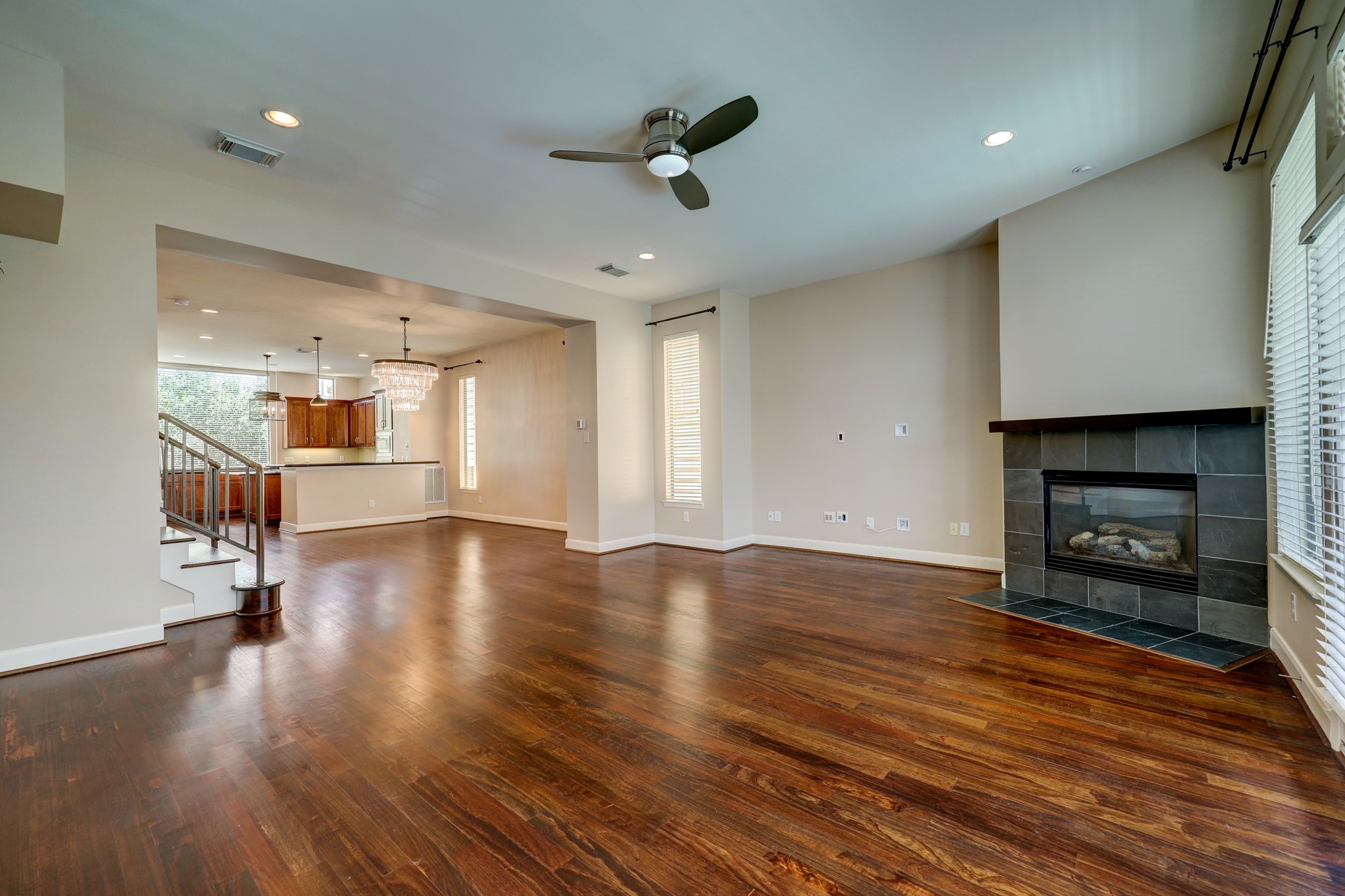 5202 Rose Street, Unit B Houston, TX 77007 - Photo 22 of 40 This spacious living area features rich hardwood floors, a modern ceiling fan, and a cozy fireplace. It seamlessly connects to an open kitchen with elegant lighting and a staircase leading upstairs, creating a welcoming and functional space.