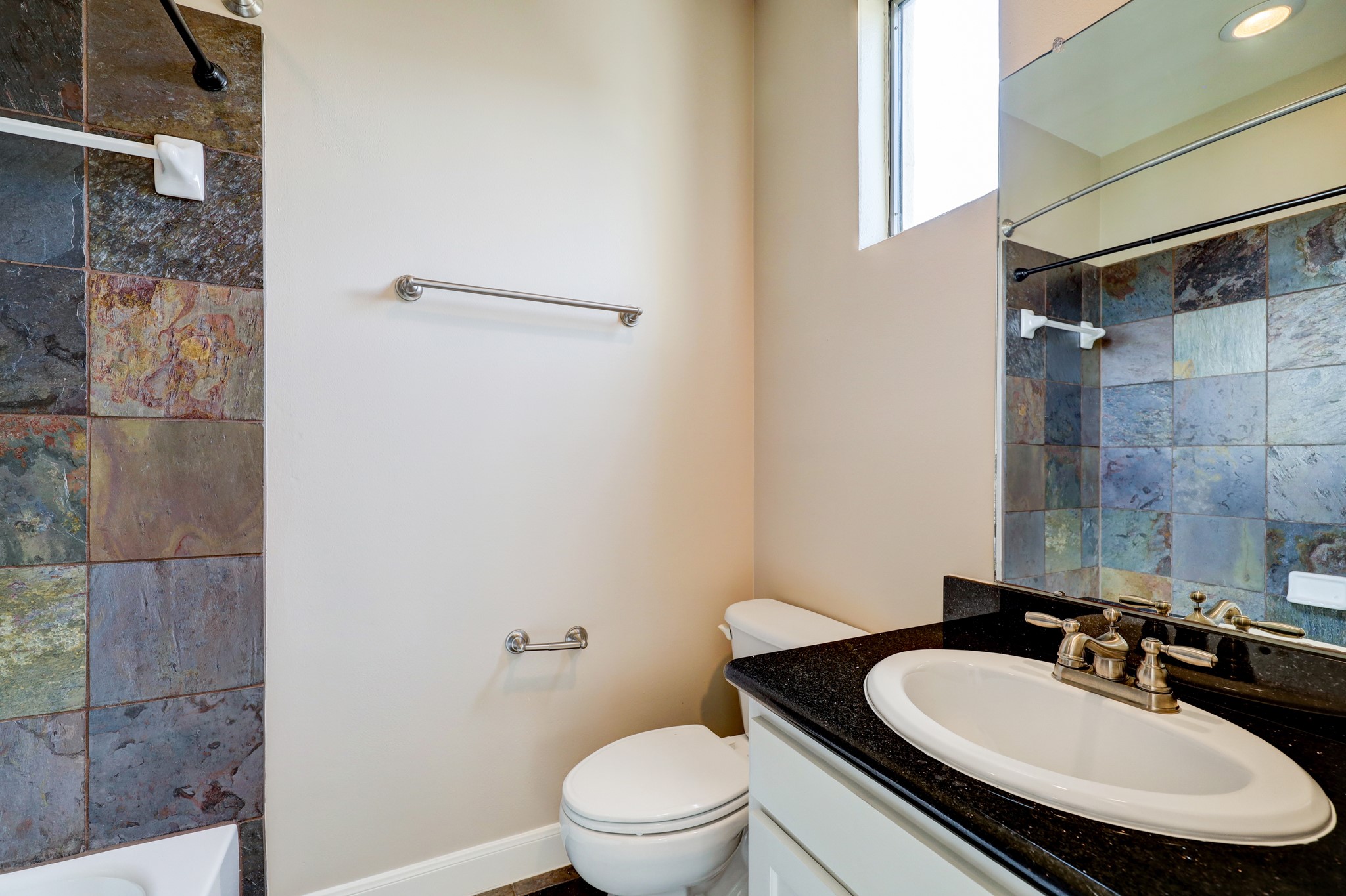5202 Rose Street, Unit B Houston, TX 77007 - Photo 23 of 40 This bathroom features a modern design with slate tile walls, a sleek black countertop, and a large mirror. It includes a bathtub, toilet, and a window for natural light.