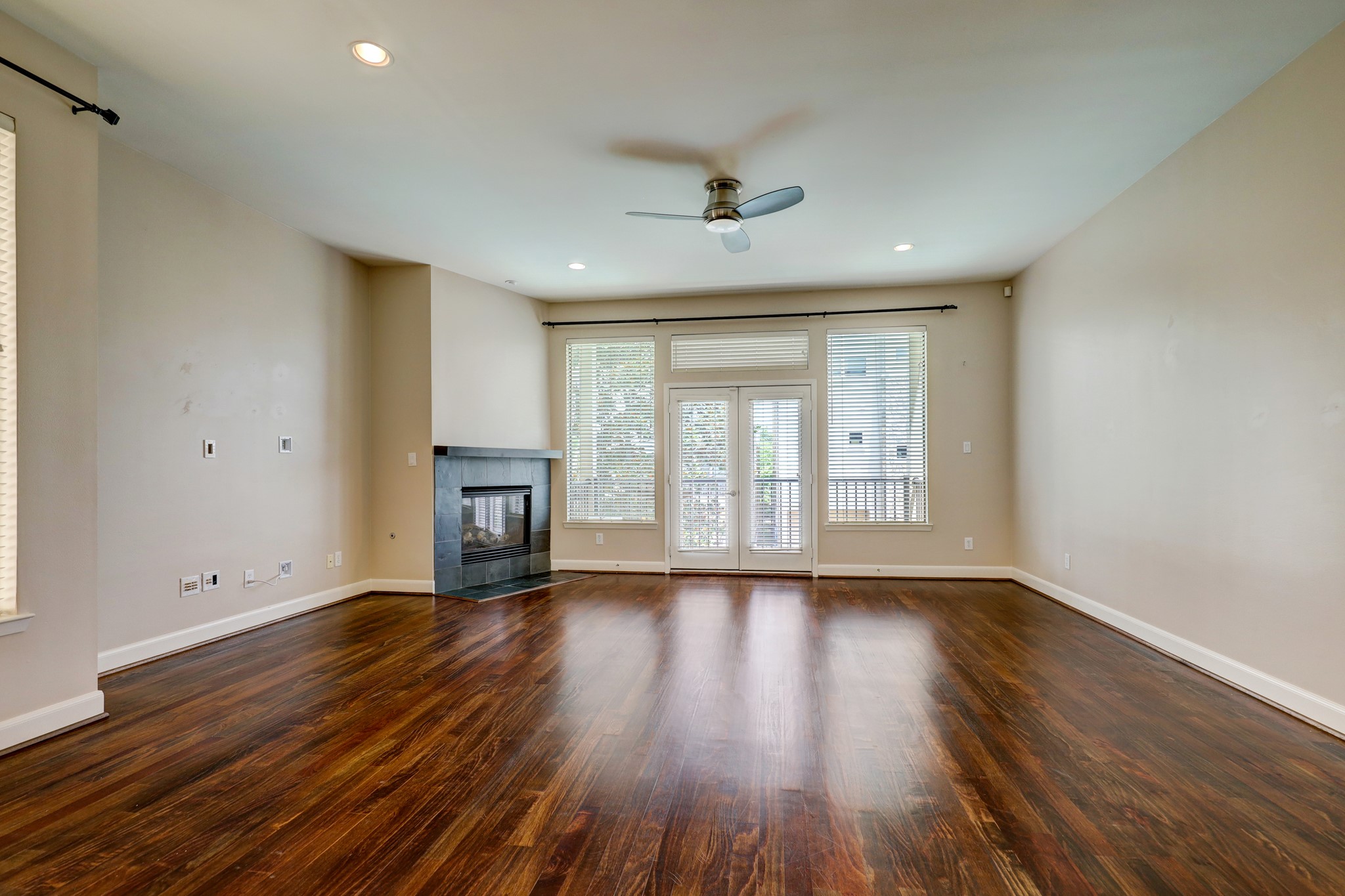 5202 Rose Street, Unit B Houston, TX 77007 - Photo 25 of 40 This spacious living room features rich hardwood floors, a modern ceiling fan, and a sleek corner fireplace. Natural light streams through large windows and French doors, leading to a balcony.