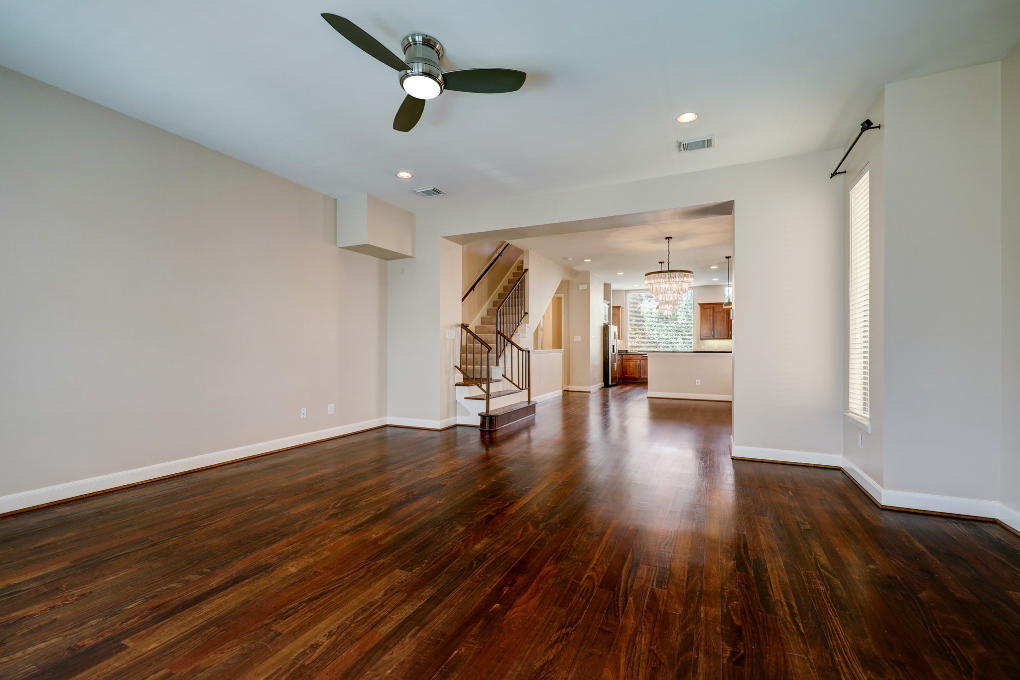 5202 Rose Street, Unit B Houston, TX 77007 - Photo 30 of 40 This spacious living area features rich hardwood floors, a modern ceiling fan, and ample natural light. It seamlessly connects to an open kitchen with a stylish chandelier and a view of the staircase, creating a warm and inviting atmosphere.