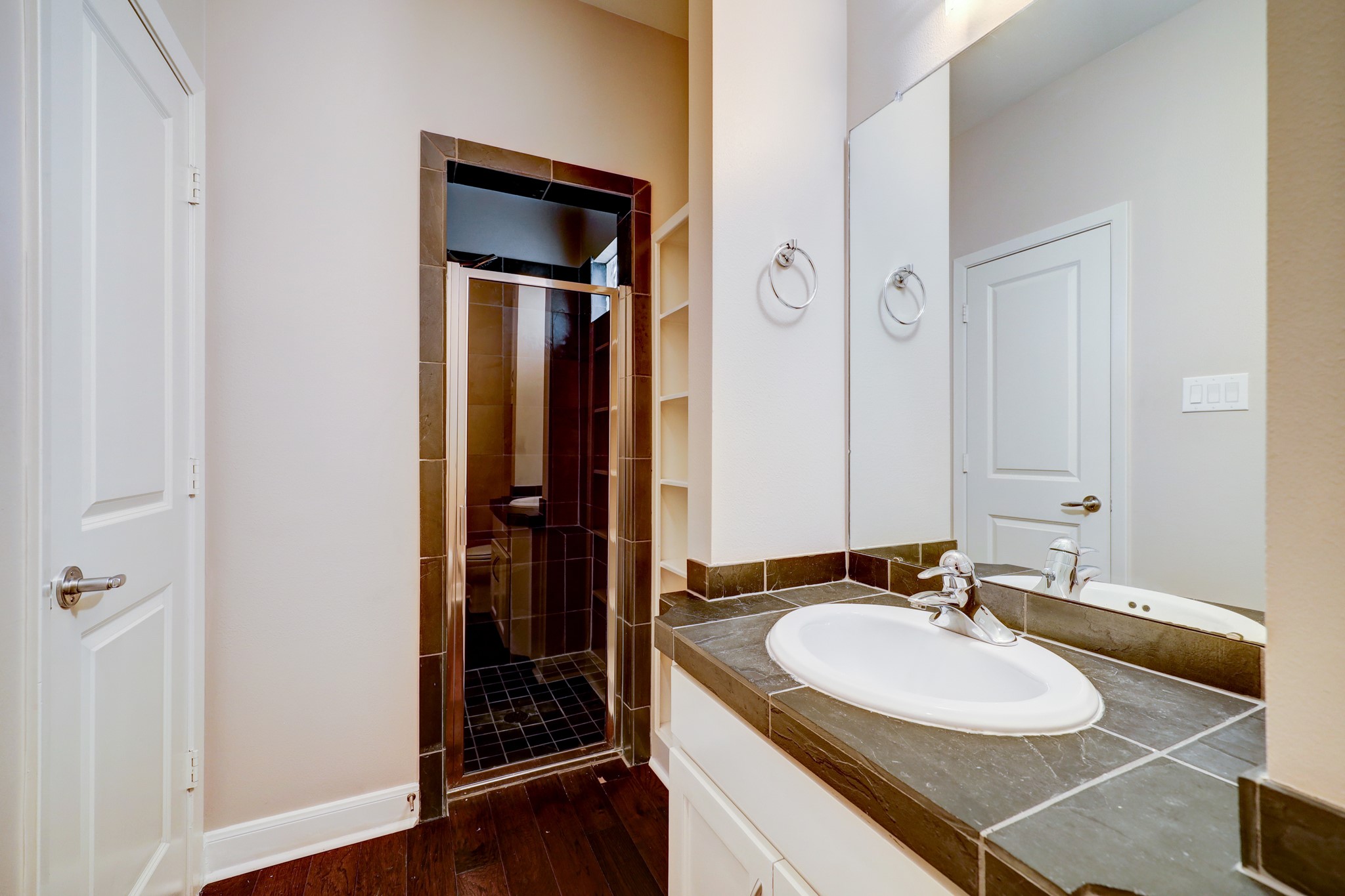 5202 Rose Street, Unit B Houston, TX 77007 - Photo 32 of 40 This modern bathroom features a sleek walk-in shower with dark tiles, a large mirror, and a stylish vanity sink. Ample storage is available with built-in shelves and a cabinet.