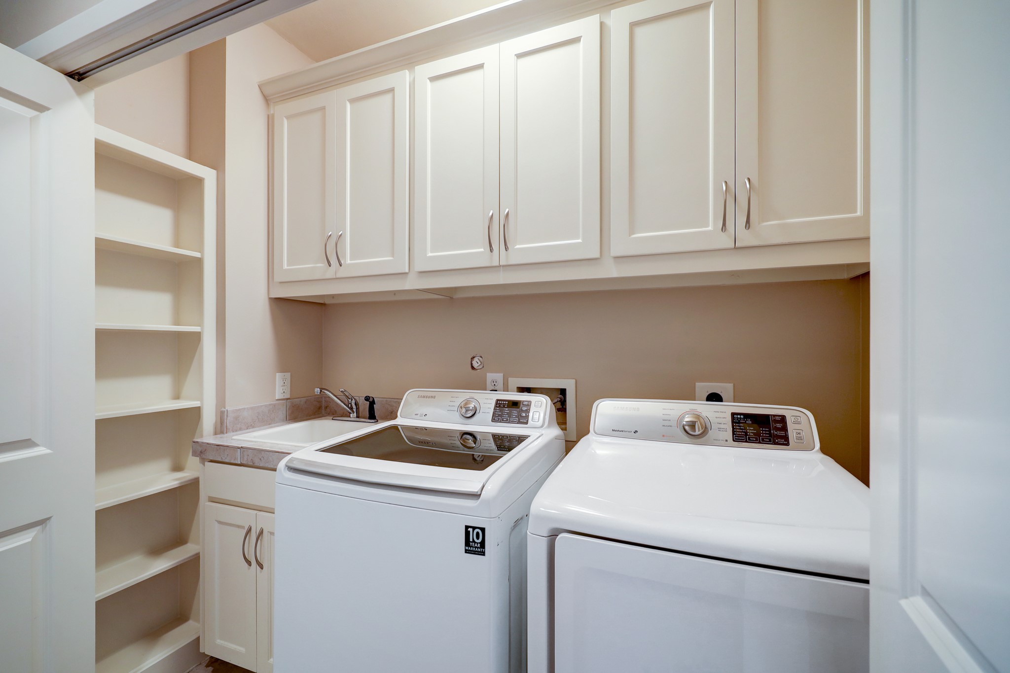 5202 Rose Street, Unit B Houston, TX 77007 - Photo 36 of 40 This photo shows a compact laundry room with a modern washer and dryer, ample cabinet storage above, and a utility sink with counter space. Built-in shelves provide additional storage options.