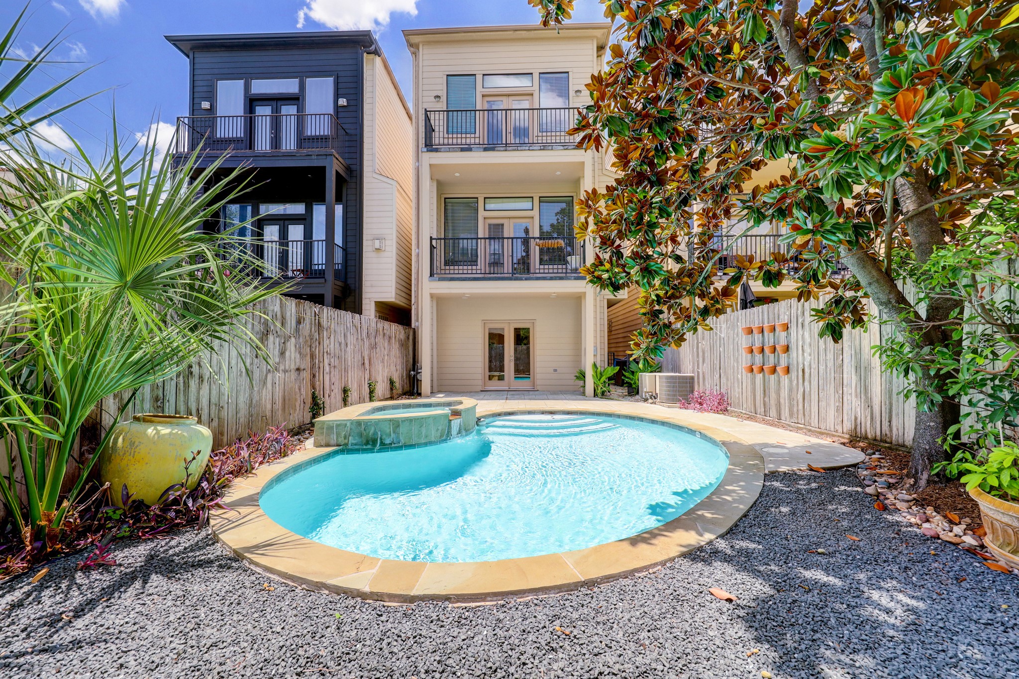 5202 Rose Street, Unit B Houston, TX 77007 - Photo 4 of 40 This inviting backyard features a modern, three-story home with balconies overlooking a private pool and spa. The space is enclosed by a wooden fence, surrounded by lush greenery and decorative plants, creating a serene oasis for relaxation.