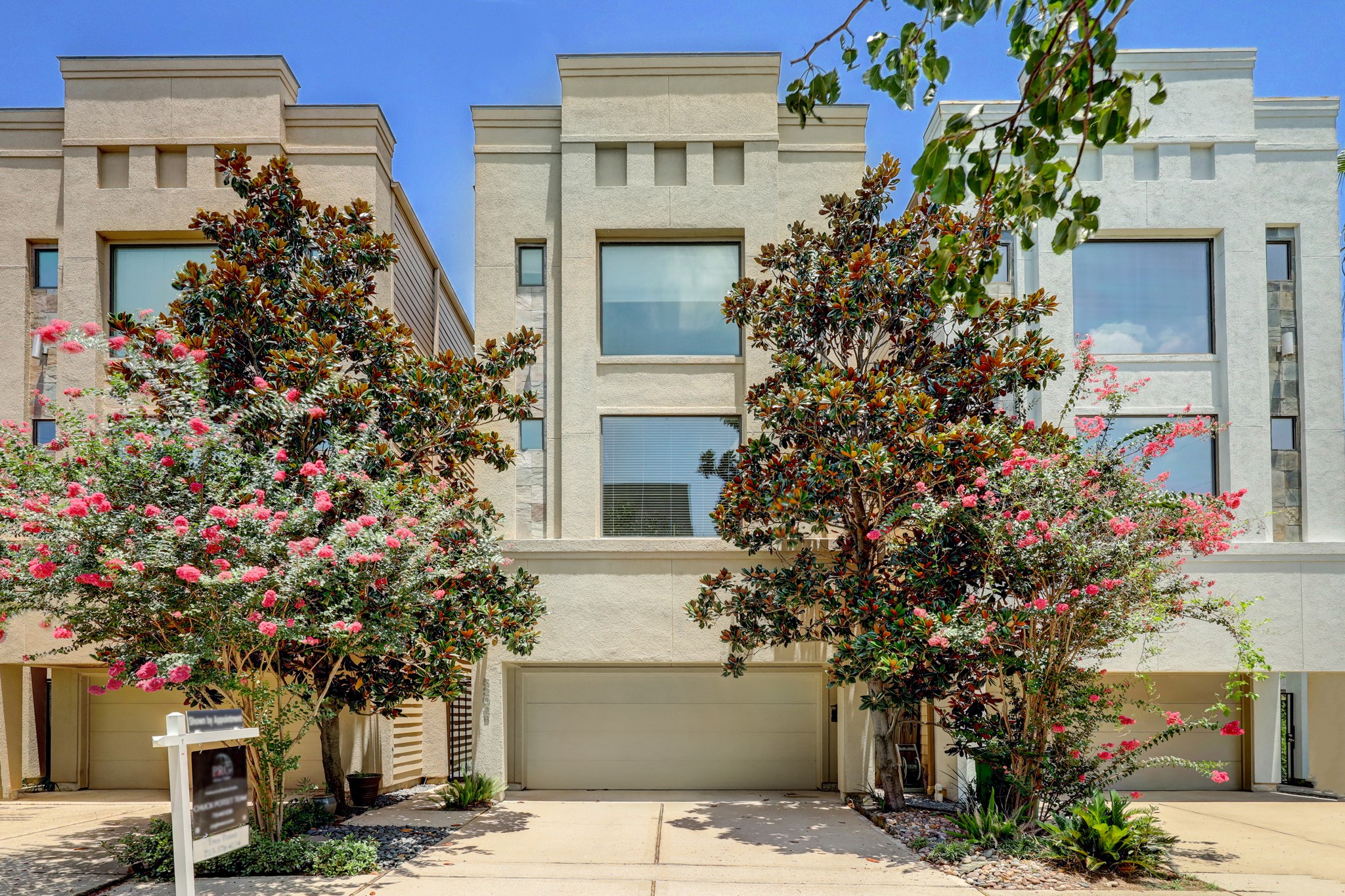5202 Rose Street, Unit B Houston, TX 77007 - Photo 5 of 40 This modern townhouse features a clean, stucco exterior with large windows and a two-car garage. The landscaped front yard includes mature trees and vibrant flowering plants, offering great curb appeal.