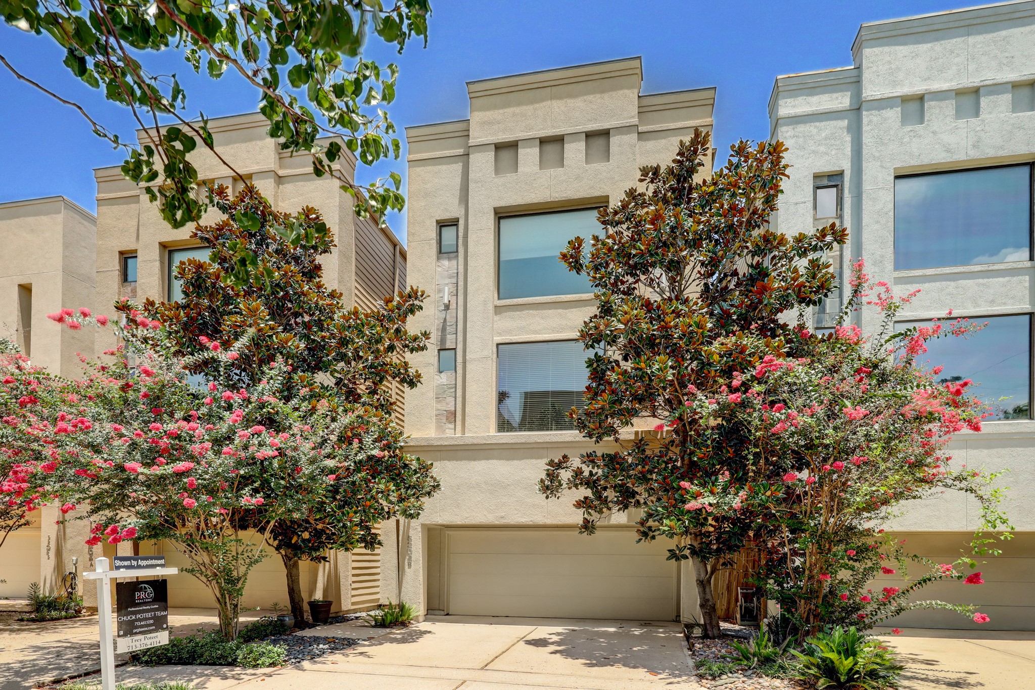 5202 Rose Street, Unit B Houston, TX 77007 - Photo 6 of 40 This modern townhouse features a clean, stucco exterior with large windows. It has a two-car garage and is framed by mature trees with vibrant pink blossoms, offering a welcoming, natural curb appeal.