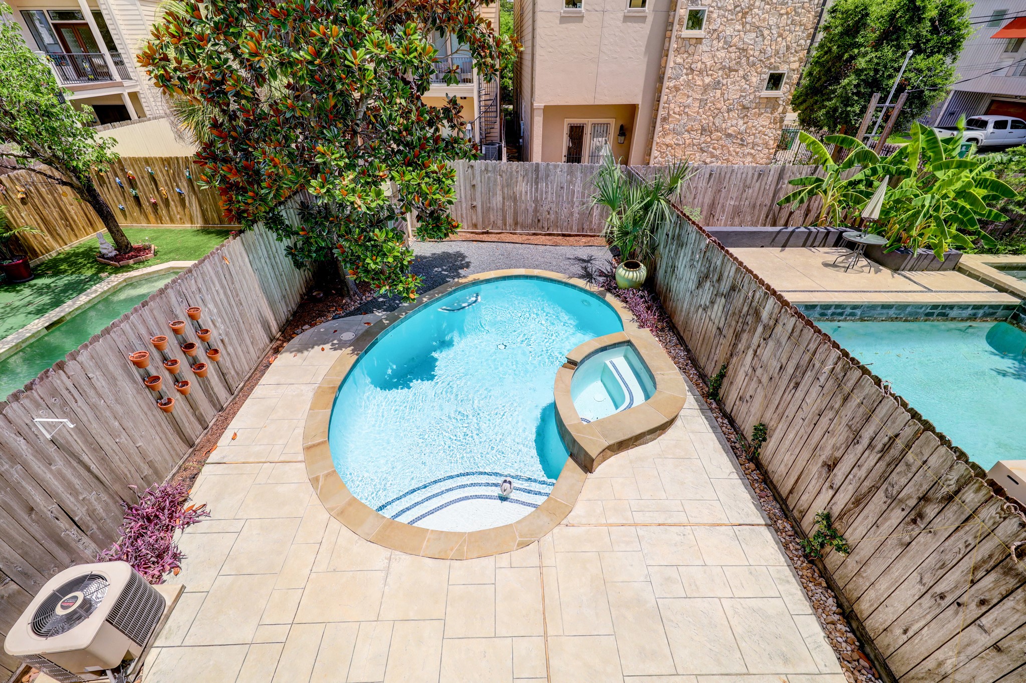 5202 Rose Street, Unit B Houston, TX 77007 - Photo 7 of 40 This photo showcases a cozy backyard with a small, oval-shaped pool and attached spa. The area is enclosed by a wooden fence, with tasteful landscaping including a tree and potted plants. There’s also a neatly tiled poolside patio, perfect for relaxation.
