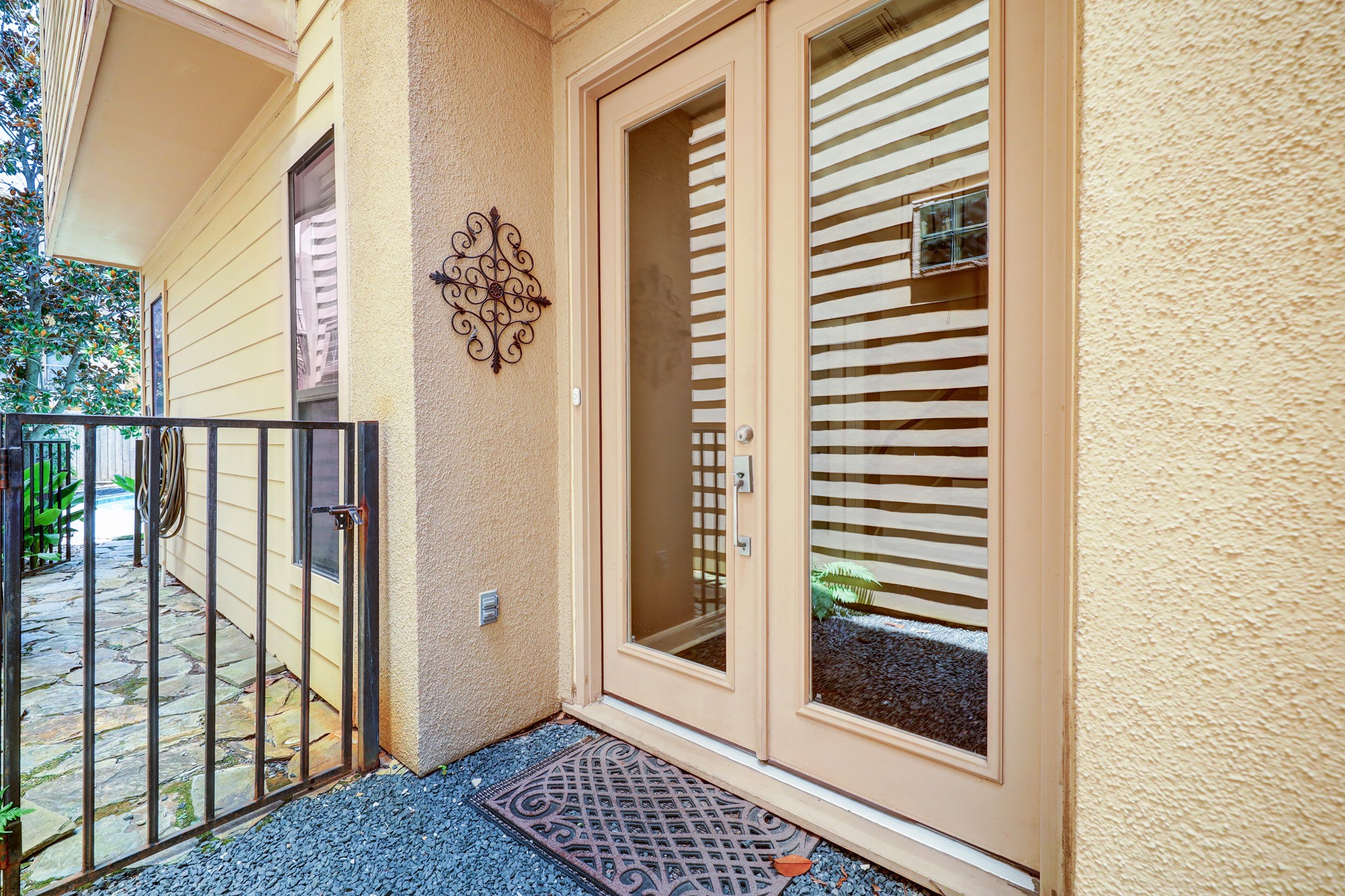 5202 Rose Street, Unit B Houston, TX 77007 - Photo 10 of 40 This photo showcases a charming entryway with double glass doors, a decorative wall ornament, and a cozy, fenced walkway with a stone path leading to the entrance.