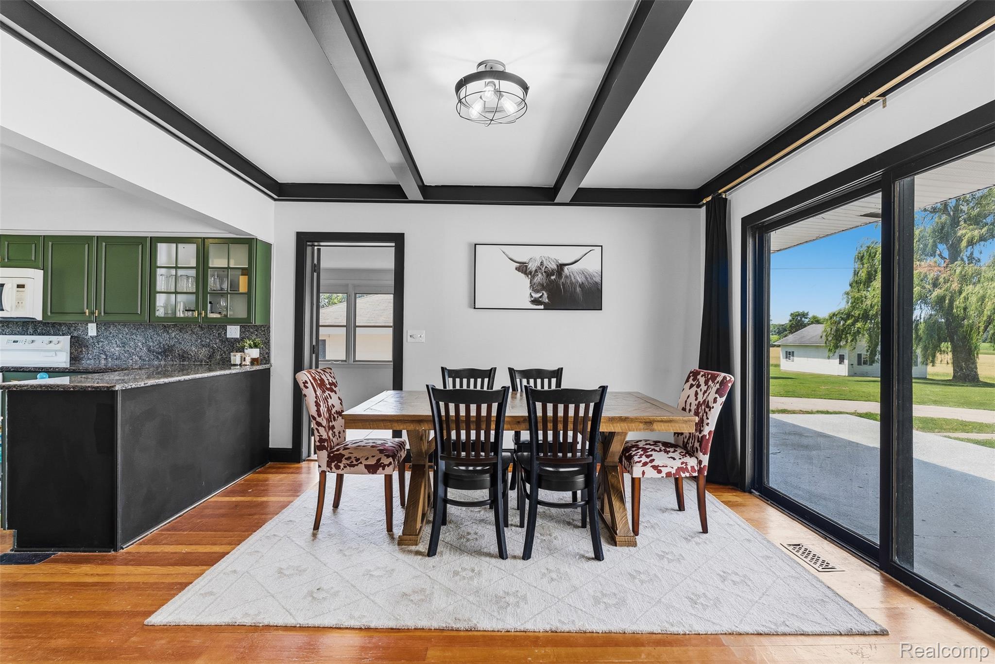 5843 West Dewey Road Owosso, MI 48867 - Photo 12 of 58 Open-concept dining area featuring wood-finish flooring, dark exposed ceiling beams, and a black-framed sliding glass door