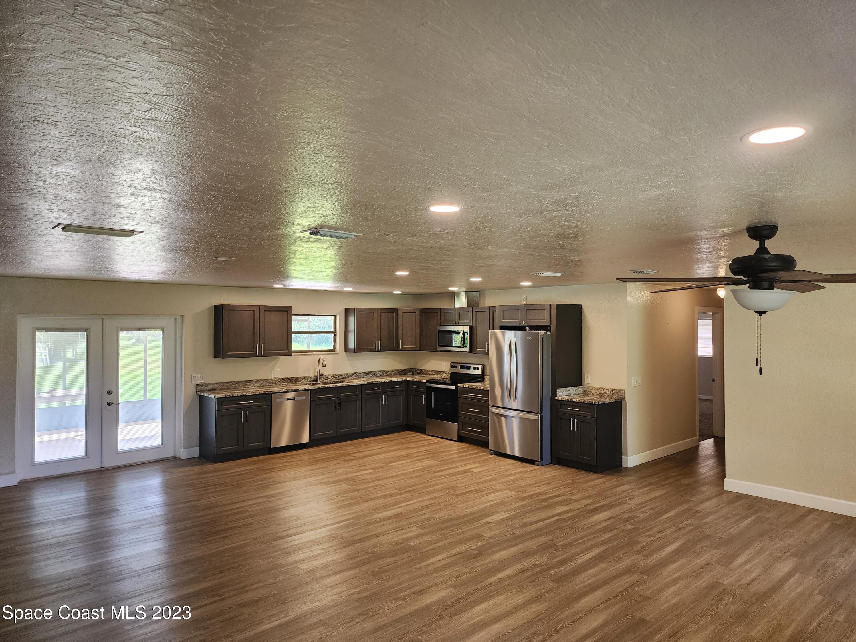 2745 Corey Road Malabar, FL 32950 - Photo 3 of 39 a kitchen with stainless steel appliances kitchen island granite countertop a refrigerator and a stove top oven with wooden floor