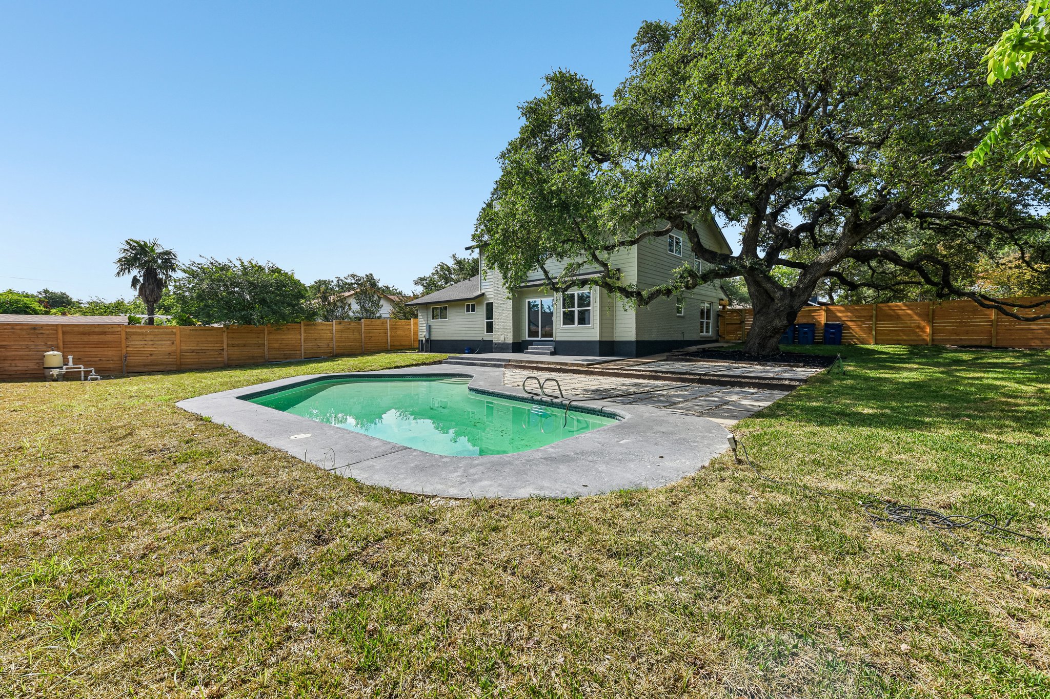 7523 Glenhill Road Austin, TX 78752 - Photo 37 of 38 A private swimming pool and patio area await, framed by a sprawling mature tree and a fenced yard.
