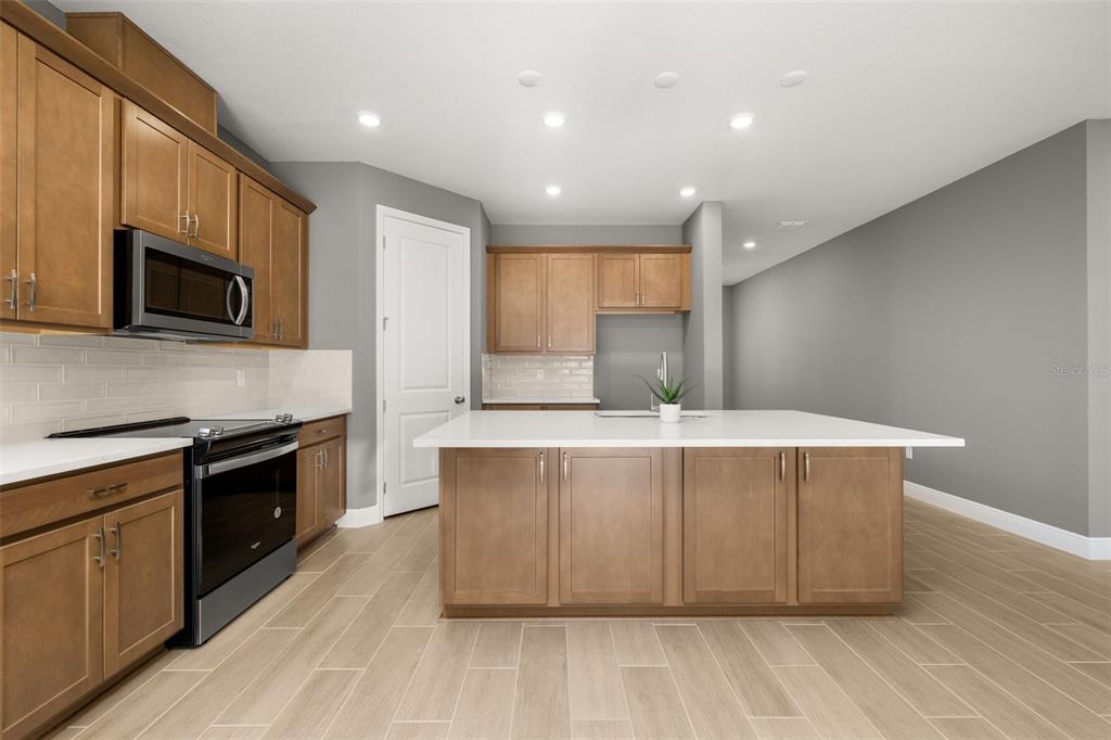 985 Fiesta Key Circle Lady Lake, FL 32159 - Photo 7 of 34 a kitchen with stainless steel appliances a stove top oven a sink dishwasher and a microwave oven with large wooden cabinets