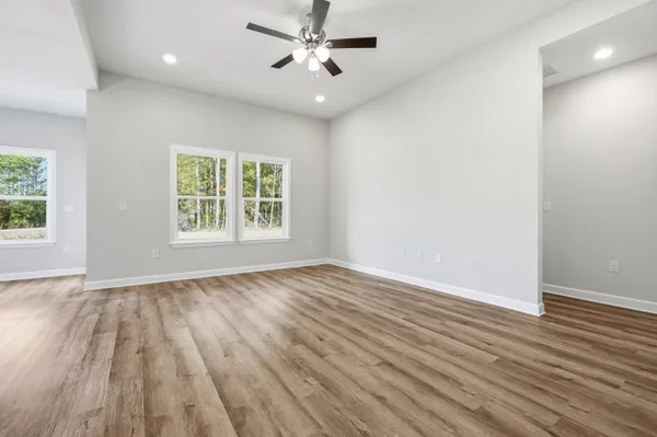an empty room with wooden floor chandelier fan and windows