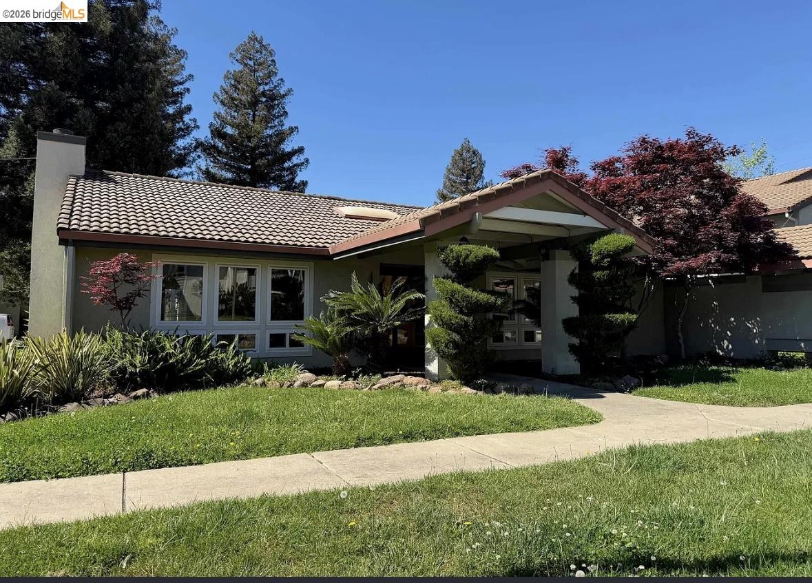 1505 Kirker Pass Road, Unit 214 Concord, CA 94521 - Photo 52 of 55 Exterior featuring a tile roof, light green stucco siding, a prominent chimney, a large picture window, and a covered entry with manicured shrubbery