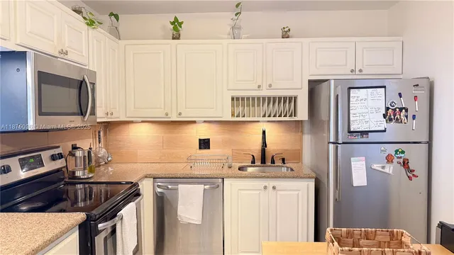 a kitchen with stainless steel appliances granite countertop a refrigerator a sink a stove and white cabinets